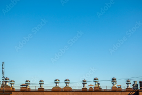 Row of chimneys are lined up on a roof. The sky is clear and blue. The chimneys are all the same size and shape