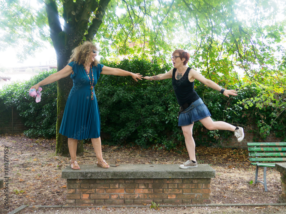 Naklejka premium Two Women Holding Hands Standing on a Brick Platform in a Park Enjoying a Sunny Day Together