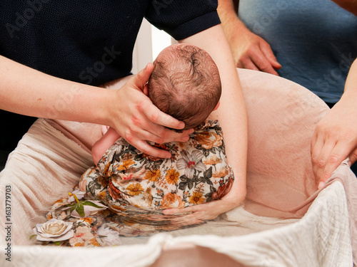 Bain thérapeutique pour nouveau-né, tenu avec douceur par un adulte dans un lange fleuri, moment de soin et d’apaisement
