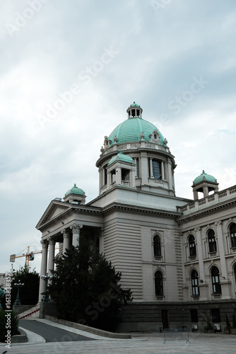 The National Assembly of the Republic of Serbia in Belgrade. A historic government building with green domes and neoclassical architecture under a cloudy sky.