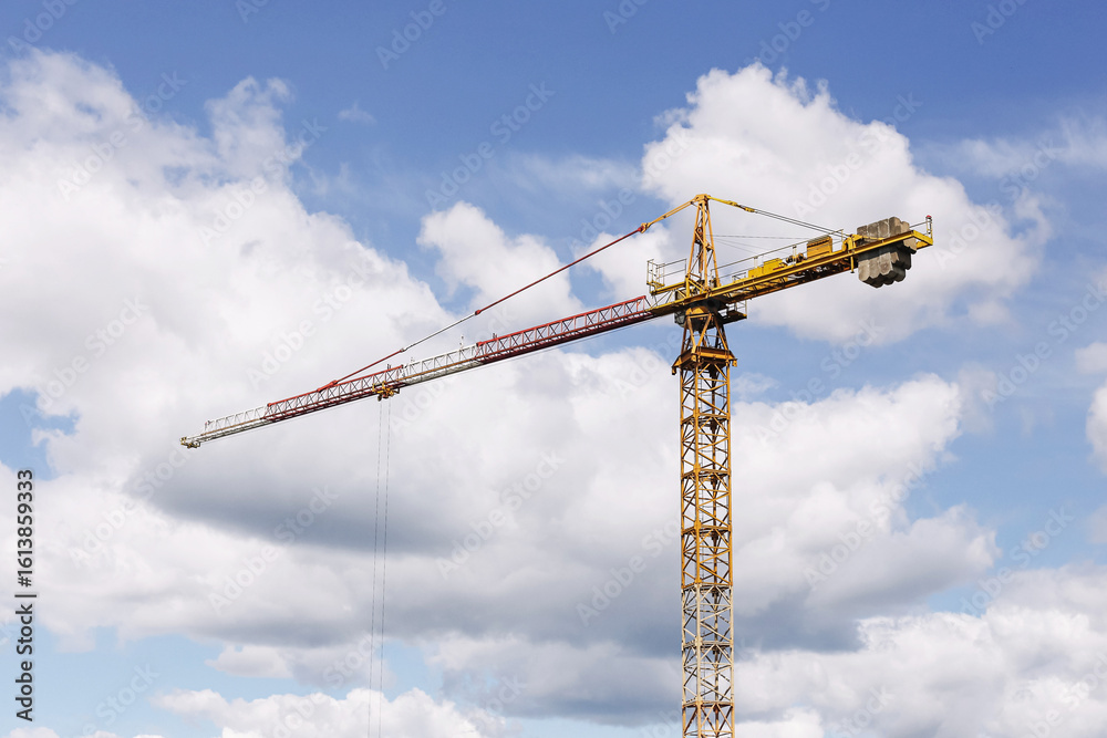 Construction crane against sky. Tower crane on building site. Industrial machinery on blue sky background. Heavy equipment in use. Large yellow crane arm. Urban development under construction. Construction crane against sky. Tower crane on building site. Industrial machinery on blue sky background. Heavy equipment in use. Large yellow crane arm. Urban development under construction.