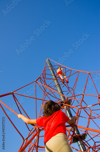 Red metal tower structure with a girl climbing under bright blue sky, capturing bold geometry and energy in abstract architectural urban space with dynamic upward composition.
