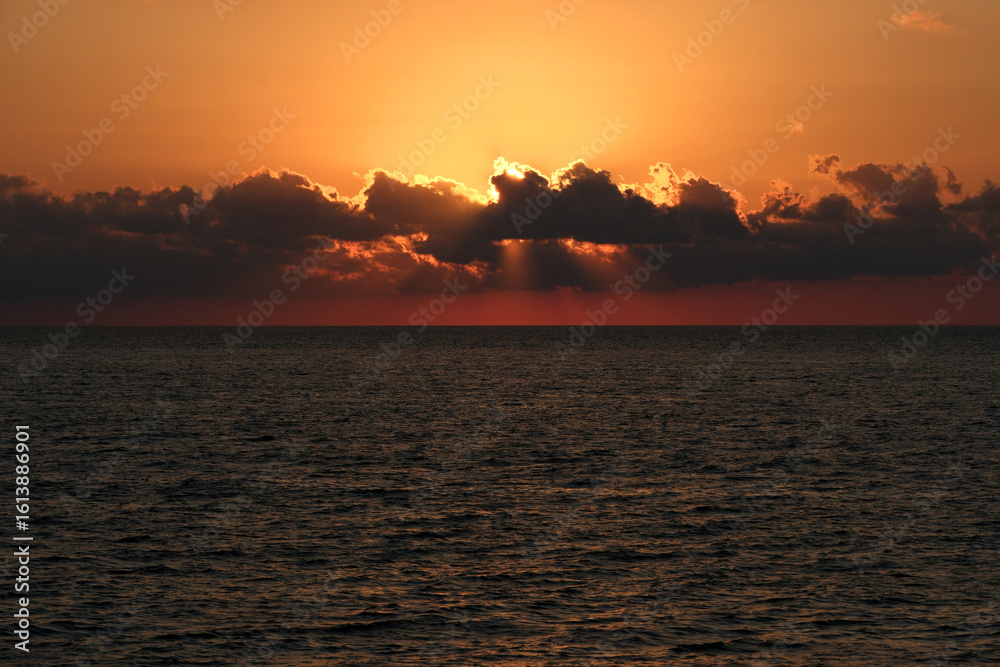 Naklejka premium Beautiful sunset over the sea. The rays of the sun break through the clouds. Sunset over the sea with clouds and rays of the sun.