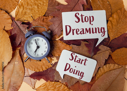 Alarm clock on autumn leaves with motivational quotes encouraging action and productivity