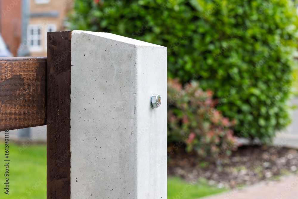 Fototapeta premium Close-up of a concrete fence post with a bolt securing a horizontal wooden panel. Common in modern garden fencing for durability, support, and property boundaries in residential areas