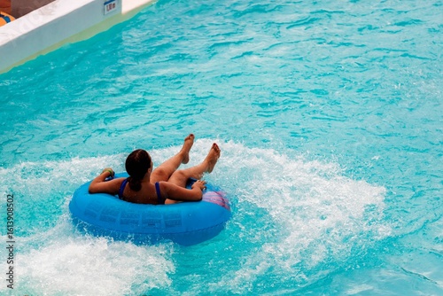A woman floats on a blue inflatable tube in the wave pool. She is enjoying the splashes of water under the Florida sun, and she is having a blast at the Orlando waterpark