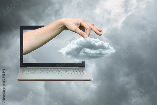 Hand reaching from laptop creating digital cloud