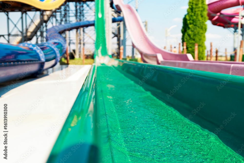 Obraz premium Aqua streams cascade through a verdant water slide at a vibrant park on a sunny day. Colorful slides twist into the distance, a playground for thrill-seekers ready for a cool escape