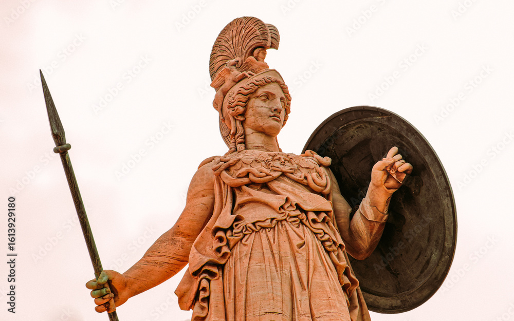 Obraz premium Statue of Athena, the Greek goddess of wisdom and knowledge, with a helmet on a gold gilded column. Elegant craftsmanship highlights the power of the deity, set against a timeless backdrop.