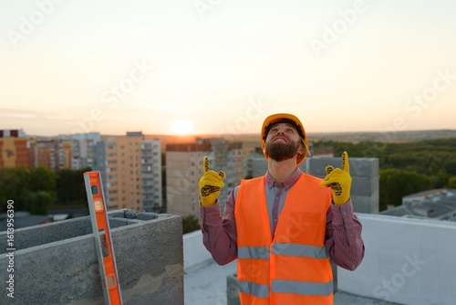Construction worker pointing upwards at building site with cranes and cityscape