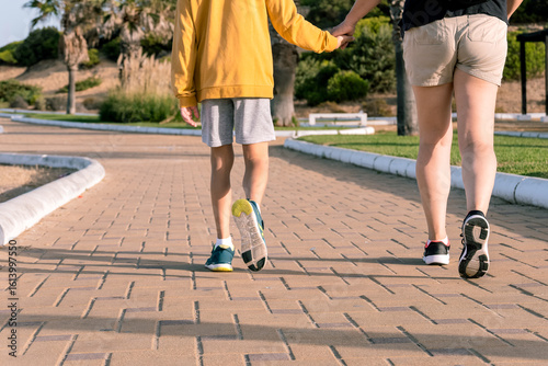 Fotografie Woman walking hand in hand with her son through a green park pathway