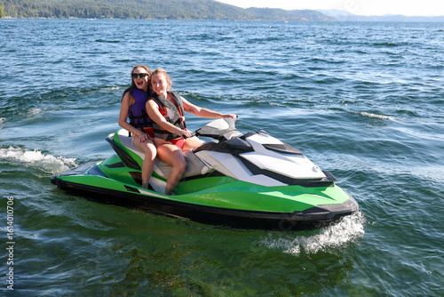 Two young women having fun on Couer D'Alene lake in Idaho riding the water on a fast jet ski watercraft outside on a long summer day. The sisters are laughing and enjoying the family time together. 