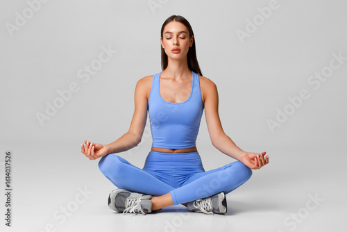 Fitness woman practicing yoga in lotus pose. Female sitting in meditation on the gray background