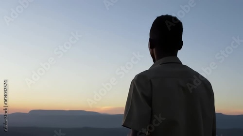 A young Black man watches the beautiful sunrise over the mountains in a peaceful and contemplative mood