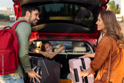 Obraz na plátně Parents packing luggage in trunk of car with kid girl sitting on backseat and lo