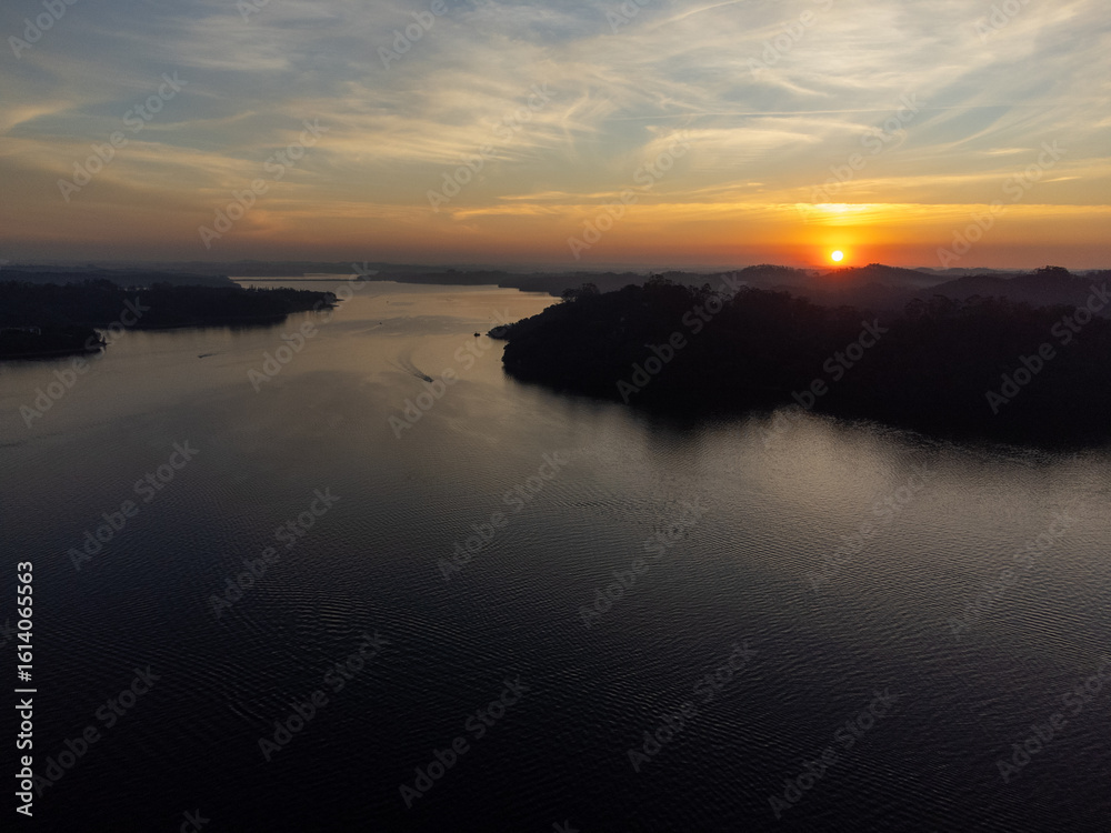 Obraz premium Orange sun setting between mountains behind large lake