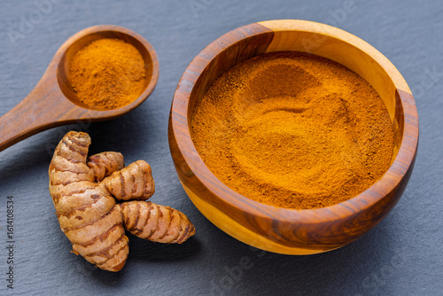 Fototapeta Naklejka Na Ścianę i Meble -  Turmeric roots and powder in a wooden bowl on a dark slate board: natural superfood and culinary spice
