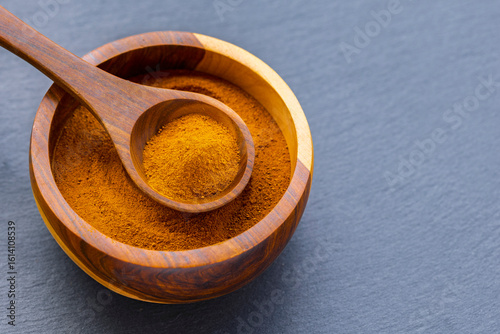 Fototapeta Naklejka Na Ścianę i Meble -  Turmeric roots and powder in a wooden bowl on a dark slate board: natural superfood and culinary spice