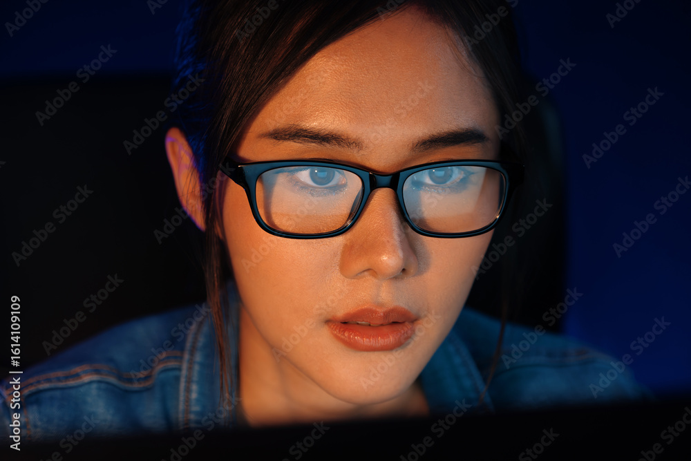 Fototapeta premium Portrait young beautiful Asian creative with glasses of serious face looking on pc to search project creator social media online, planning strategy creator at neon modern office at night. Stratagem.