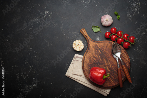 Fototapeta Naklejka Na Ścianę i Meble -  Cherry tomatoes, red bell pepper, and fresh basil leaves arranged on a rustic wooden cutting board beside a wooden pepper mill against a dark textured background, copy space