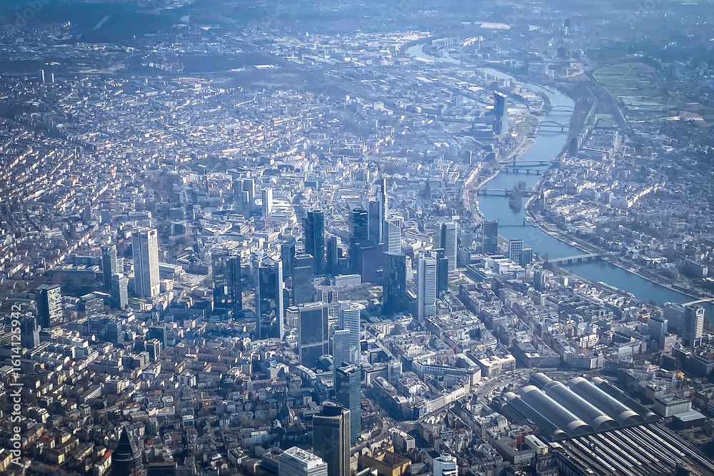 Fototapeta premium Aerial view of Frankfurt am Main, Germany, showing the skyline with high-rise buildings, the Main River, and central train station on a clear day seen from an airplane
