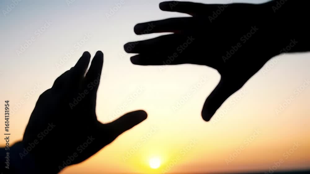 Two silhouetted hands reaching toward each other against a bright, soft sunset gradient sky from white to orange and blurred horizon Two silhouetted hands reaching toward each other against a bright, soft sunset gradient sky from white to orange and blurred horizon