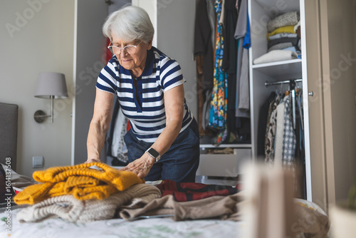 Фотография Elderly woman arranging clothes in a wardrobe in her bedroom at home