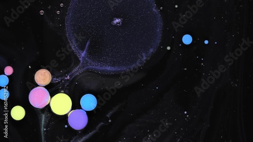 Creative process of drops of acrylic paint mixing in oil on a dark background