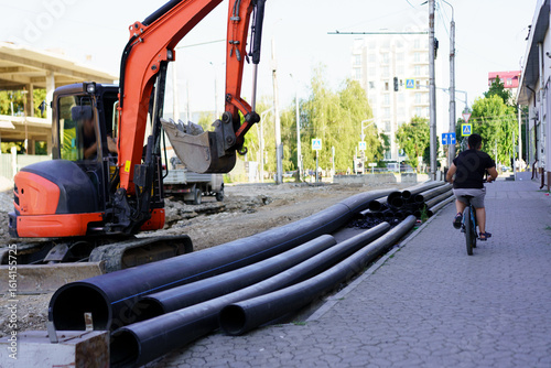 Construction site features machinery and cyclist on sidewalk in urban area during sunny day