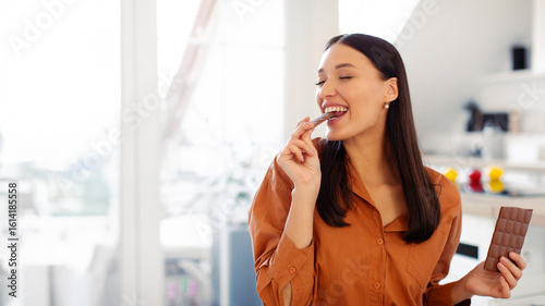 Photography Young satisfied lady eating piece of black chocolate, holding tile in her hand,