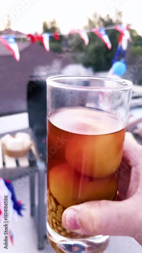Chilean Independence Day vertical video: Man holding glass of mote con huesillo in foreground with festive Chilean grill scene and flag bunting in background