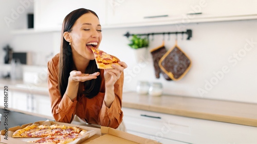 Canvas Print Excited young woman eating pizza, biting slice and enjoying its smell and taste, being satisfied with fast food delivery service