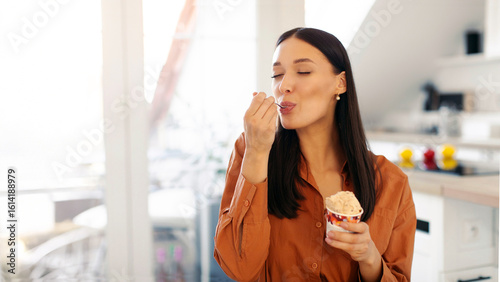 Foto Satisfied woman eating delicious ice cream with closed eyes, licking spoon, enjo