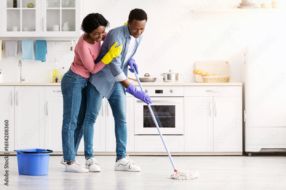 Beautiful african american young couple mopping floor in kitchen together, full length photo, copy space. Loving cheerful black lady hugging her smiling boyfriend while cleaning house Beautiful african american young couple mopping floor in kitchen together, full length photo, copy space. Loving cheerful black lady hugging her smiling boyfriend while cleaning house