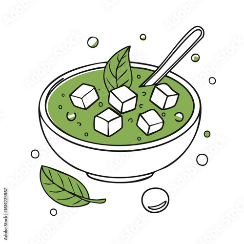 Fresh green soup with tofu cubes in a bowl with a spoon and leaves