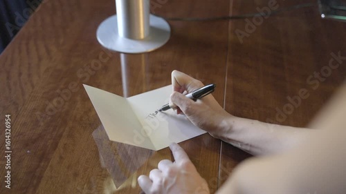 This video shows hands opening a card and writing thank you inside of it. The clip conveys gratitude, appreciation, and a personal touch.