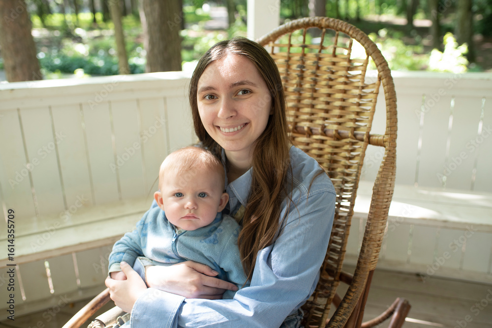 Fototapeta premium Young woman with long hair sits with baby child on rocking chair, in summer in gazebo, on sunny day. focus on the woman.
