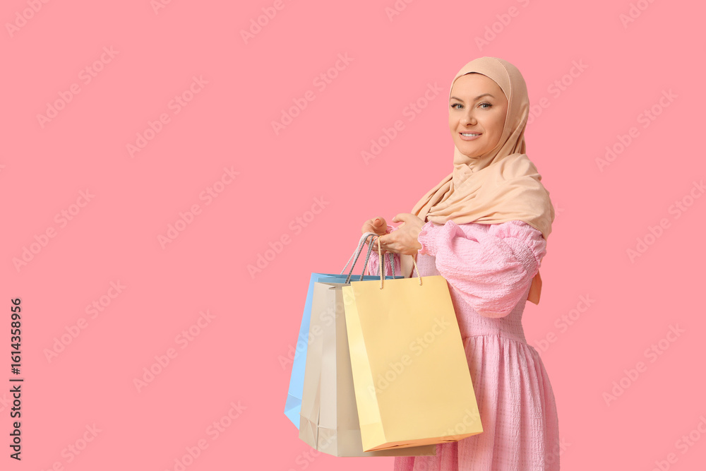Fototapeta premium Beautiful Muslim woman in hijab with shopping bags on pink background