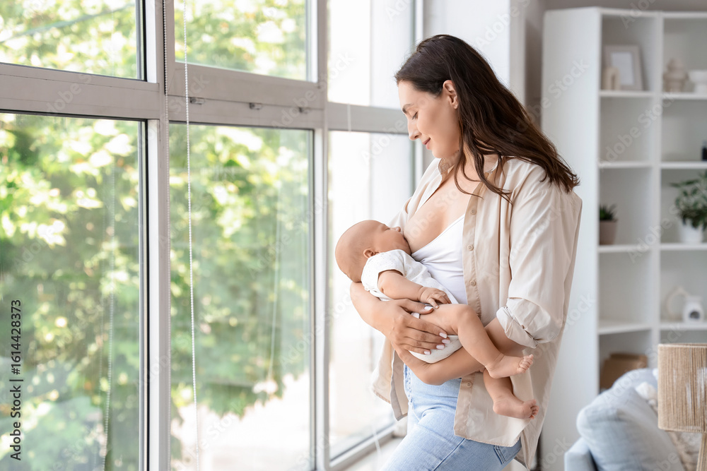 Young mother breastfeeding her baby near window at home Young mother breastfeeding her baby near window at home