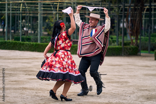 Portrait of a smiling young couple dressed as Chilean huasos,  joyfully dancing cueca outdoors. Traditional Chilean dance. Chilean traditions, celebrations.