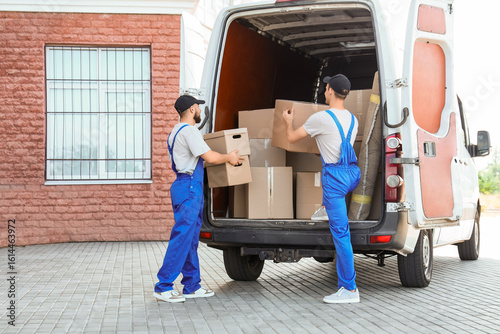 Quadro su tela Male movers unloading car with boxes on street, back view