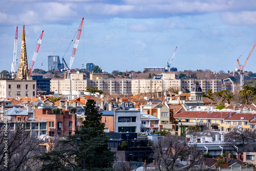 Fototapeta premium Elevated cityscape view over the rooftops of South Yarra, Melbourne, Australia, featuring a mix of historic townhouses, modern apartments, and high-rise construction cranes.