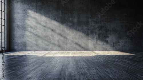 A spacious, empty room with a concrete wall and wooden floor, illuminated by natural light from a window. The room has a minimalist design with a dark color palette
