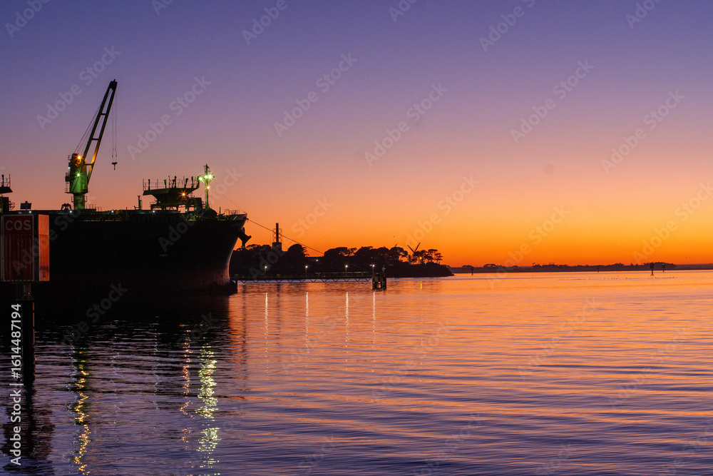 Obraz premium Ferry dock in Geelong for the Spirit of Tasmania with industrial cranes in the background as the sun sets over the Bass Strait in Victoria, Australia