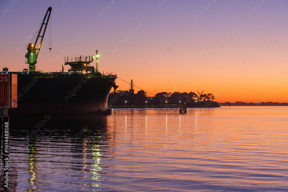 Obraz premium Ferry dock in Geelong for the Spirit of Tasmania with industrial cranes in the background as the sun sets over the Bass Strait in Victoria, Australia