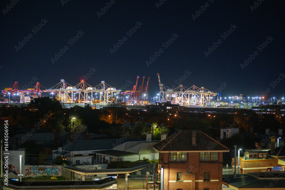 Fototapeta premium Cranes above the Melbourne sky line with Footscray Train Station in the foreground at night photographed in June 2025 from a nearby car park