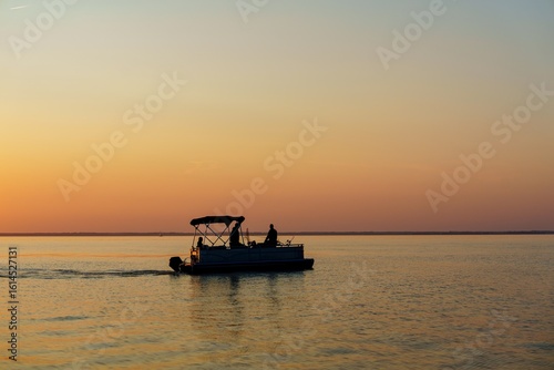 Tableau sur toile A tranquil sunset fishing scene on the Baltic Sea, featuring a silhouetted pontoon boat against vibrant dusk colors