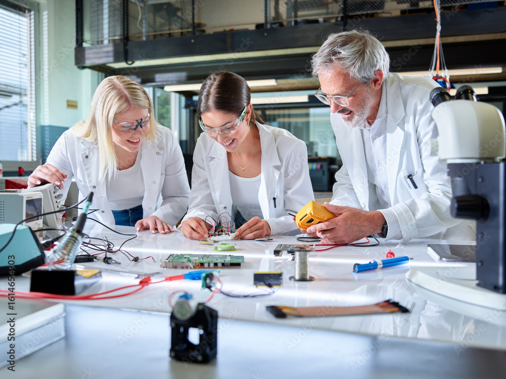 Happy professor with trainees working on circuit board in laboratory Happy professor with trainees working on circuit board in laboratory
