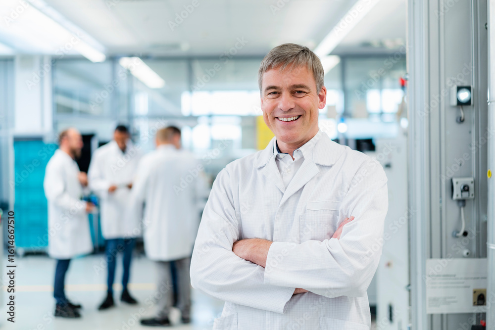 Technician in white lab coat standing in electronics factory with arms crossed Technician in white lab coat standing in electronics factory with arms crossed