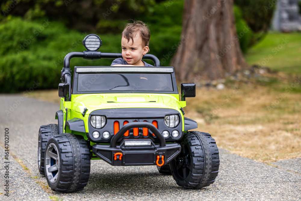 Fototapeta premium Young Toddler Driving Electric Toy Car Outdoors in Vancouver, BC